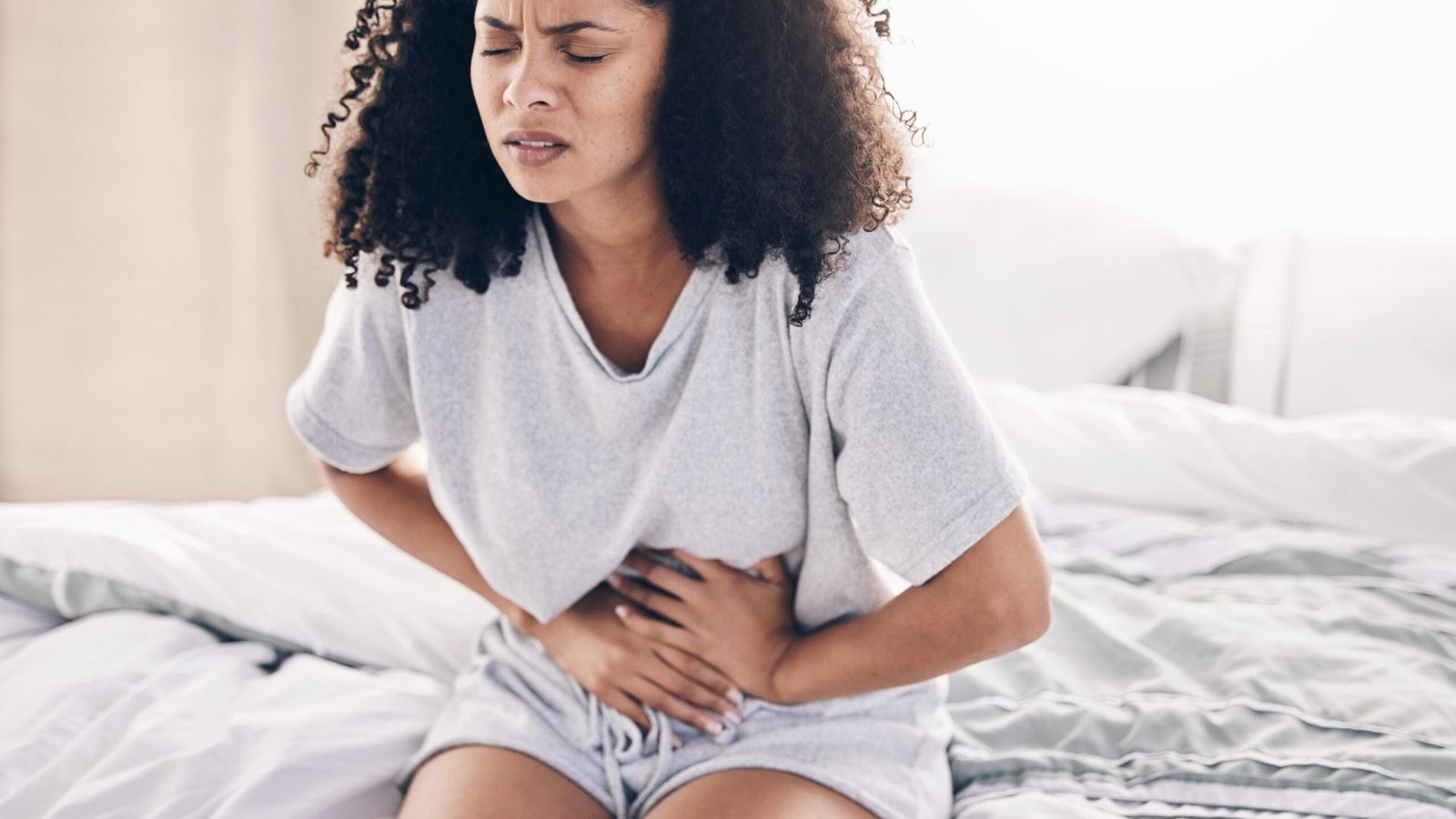 Abdomen pain, period and black woman in bed with abdominal cramps, menstruation and stomach ache. Health, medical emergency and girl with digestion problem, pms crisis and endometriosis in bedroom